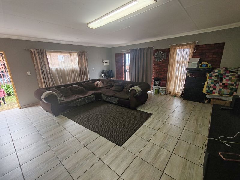 Spacious living room featuring neutral floor tiles, large windows for natural light, and a feature brick wall, offering a versatile layout for family living.