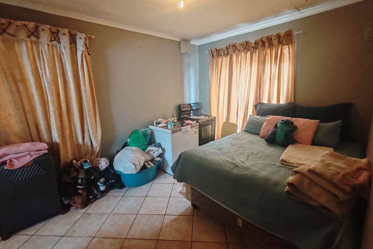 A bedroom featuring tiled flooring and dual window treatments, currently utilized with a freestanding stove present in the corner.