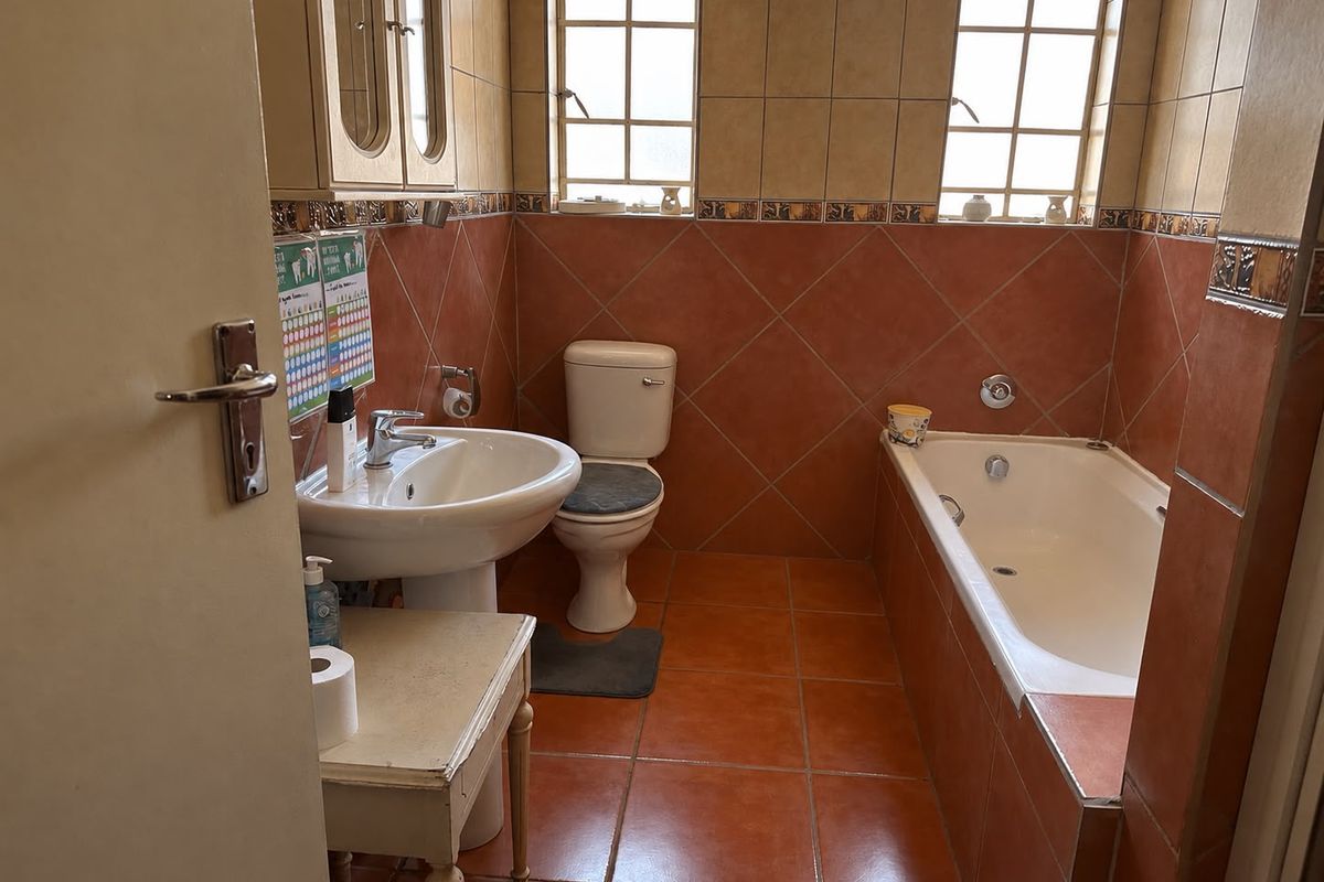 A functional bathroom featuring a built-in bathtub, pedestal sink, and toilet, finished with terracotta-style floor and wall tiles.