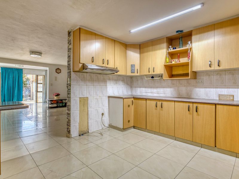 Open plan kitchen area featuring laminate cabinetry, tiled splashbacks, and tiled flooring, requiring some maintenance and cosmetic updates to the cabinetry and wall finishes.