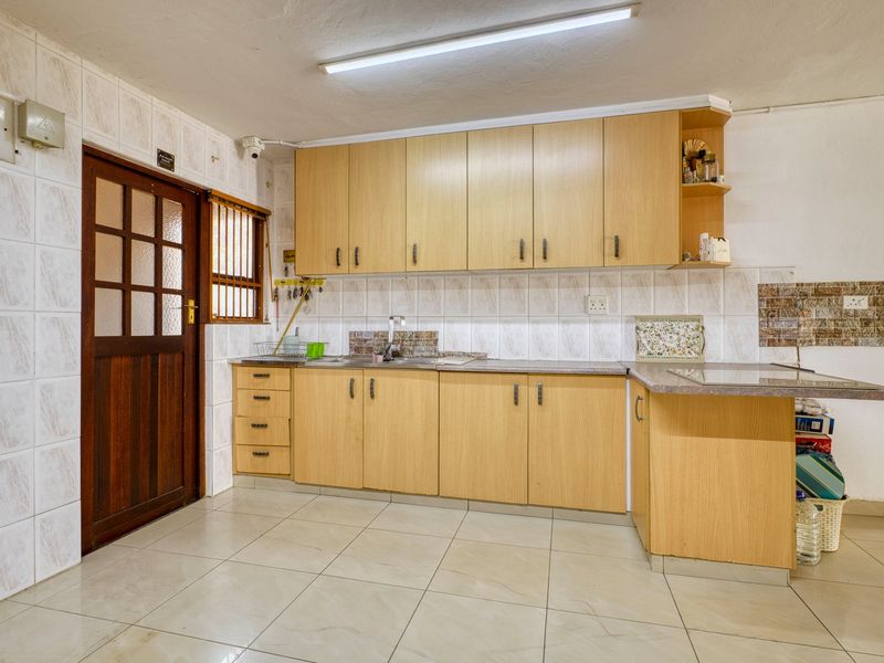 A functional kitchen featuring light wood-finish cabinetry, tiled backsplash, and ceramic flooring, providing a practical workspace with direct access to an exterior door.