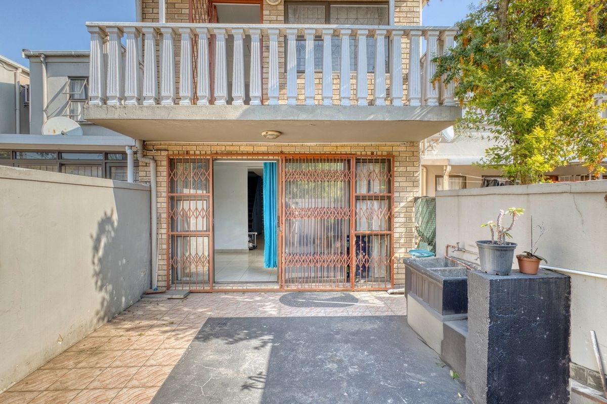Rear exterior view of the apartment featuring a paved patio, built-in wash basin, and an upper-level balcony with a classic balustrade.