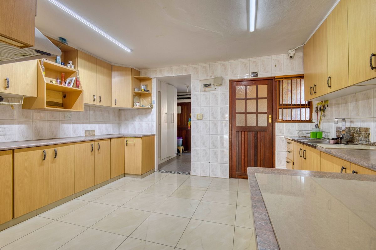 A functional kitchen featuring laminate cabinetry, tiled surfaces, and a double sink, offering a practical layout with potential for modern cosmetic updates.