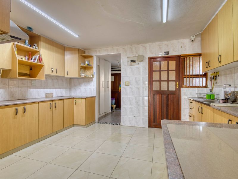 A functional kitchen featuring laminate cabinetry, tiled surfaces, and a double sink, offering a practical layout with potential for modern cosmetic updates.