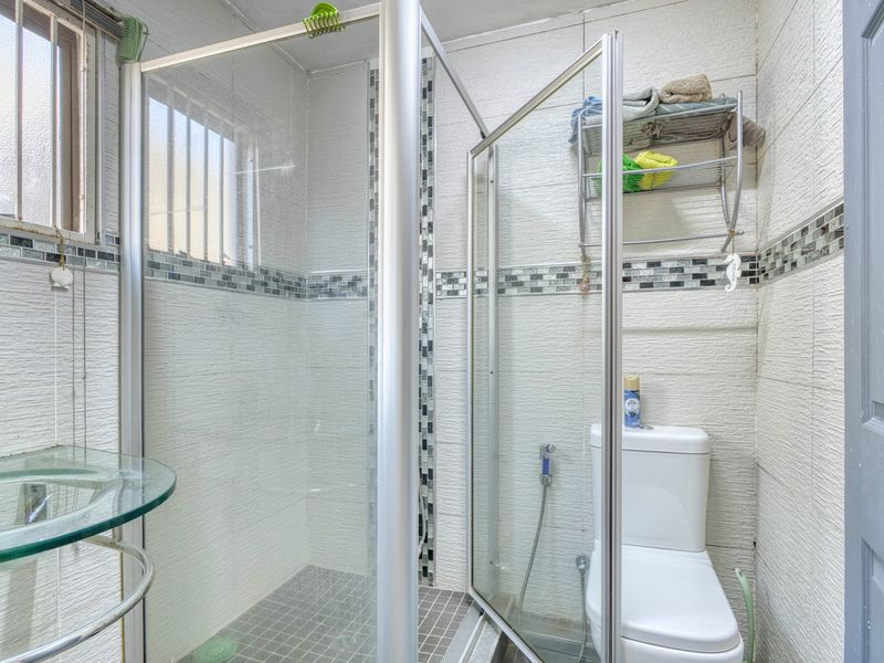 Compact bathroom featuring a glass shower enclosure, toilet, and glass vanity shelf with textured wall tiles and a decorative mosaic border.