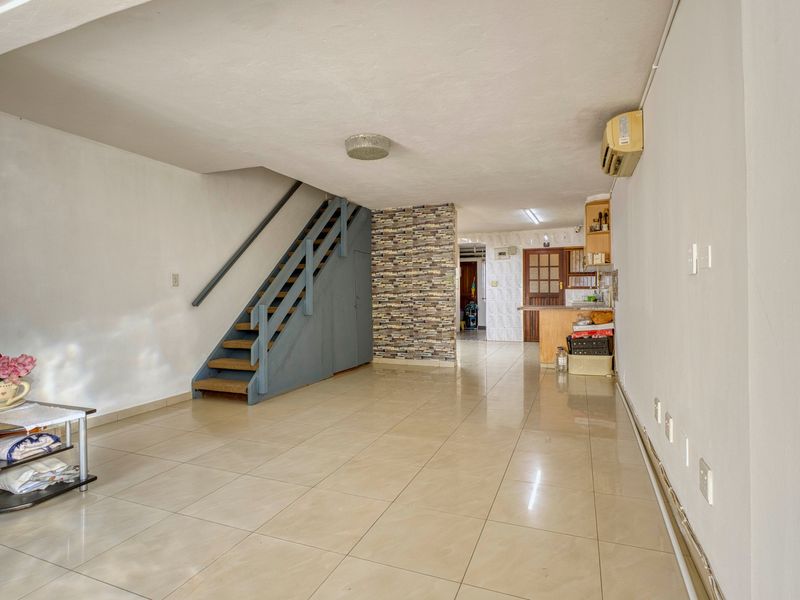 Open plan living area featuring ceramic floor tiles, a staircase with built-in storage, and a stone veneer accent wall leading to the kitchen area.