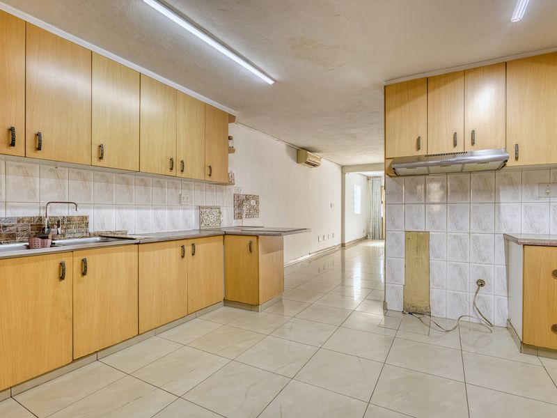 A spacious, empty kitchen featuring light wood-finish cabinetry, tiled flooring, and a tiled backsplash, offering a blank canvas for modern renovation.