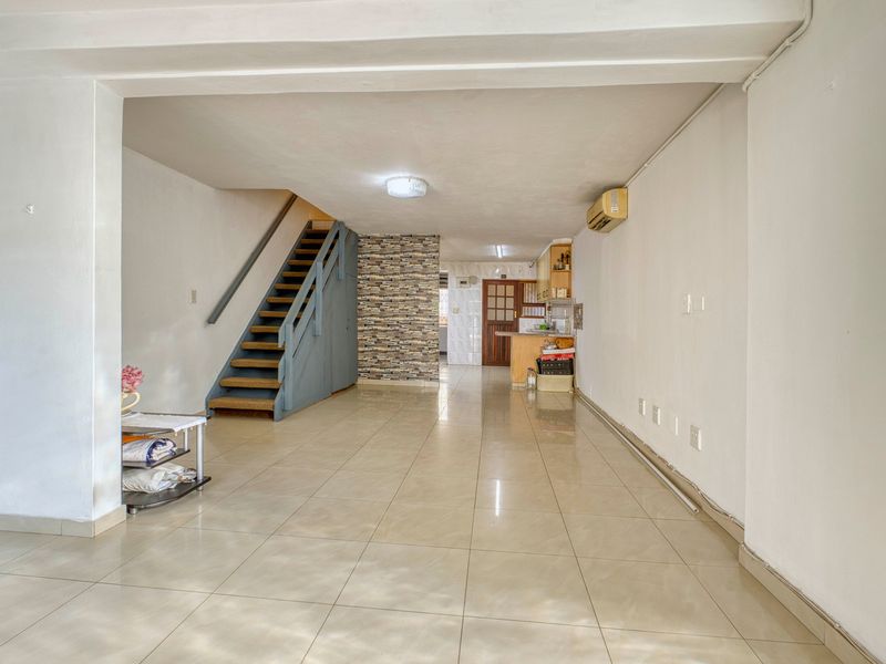 Spacious open-plan living area featuring tiled flooring, a built-in staircase, and a kitchen area with cabinetry, offering a versatile layout for modern living.