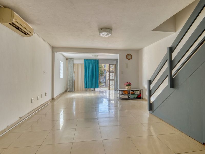Spacious open-plan living area featuring tiled flooring, a split-system air conditioner, and a staircase leading to the upper level.