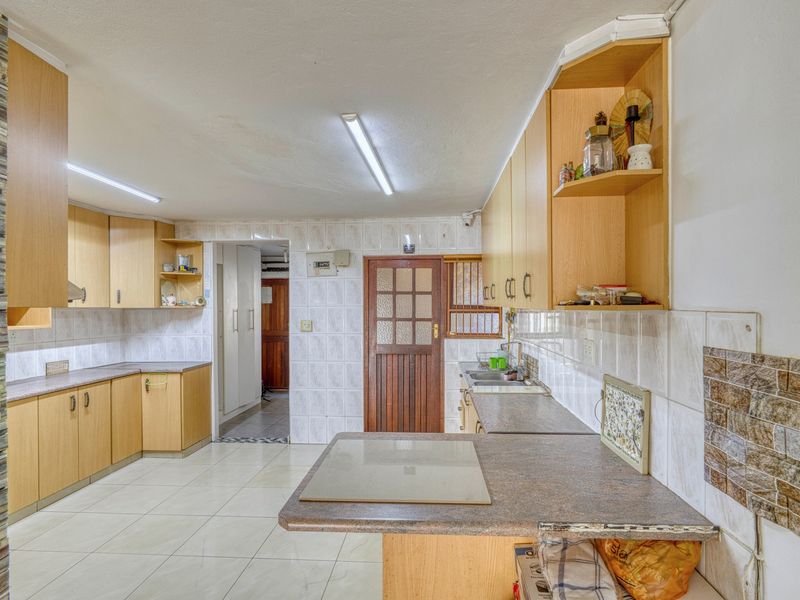 A functional kitchen featuring laminate cabinetry, tiled backsplash, and tiled flooring, offering a practical layout with ample counter space and integrated sink.