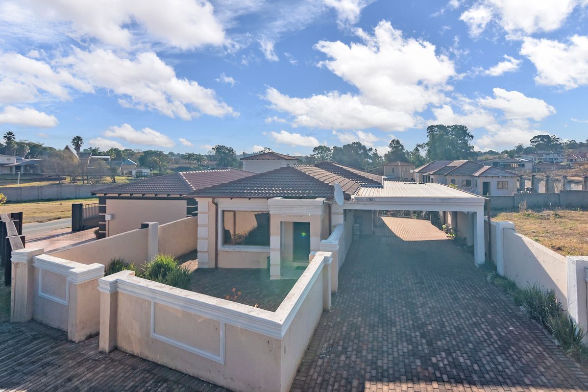 An elevated view of the property featuring a paved driveway, covered carport, and perimeter boundary walls.