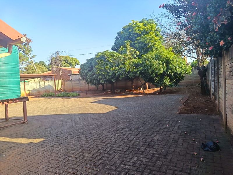 A spacious rear yard featuring extensive brick paving, a large water storage tank, and established trees enclosed by a perimeter wall.
