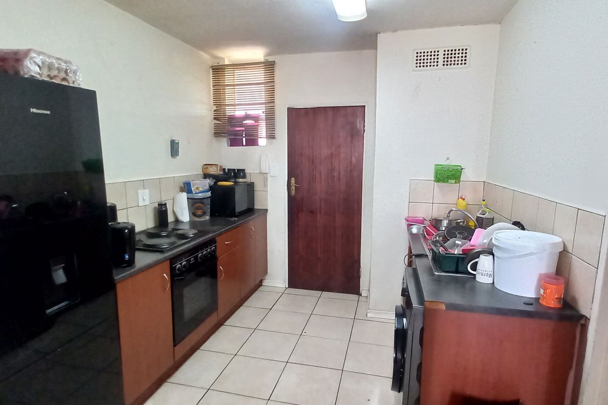 A functional galley-style kitchen featuring wood-finish cabinetry, tiled splashbacks, a built-in oven and hob, and tiled flooring.