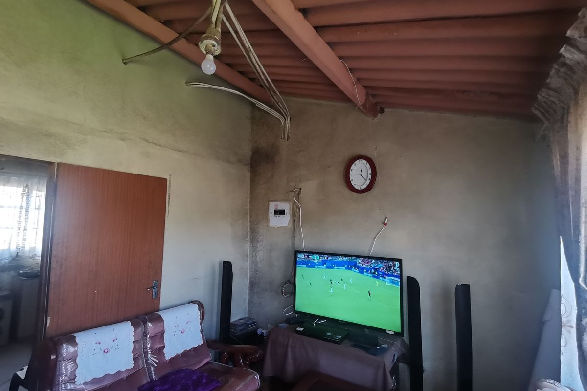 Living room area featuring exposed corrugated roofing and visible electrical conduit, requiring significant cosmetic updates and finish improvements.