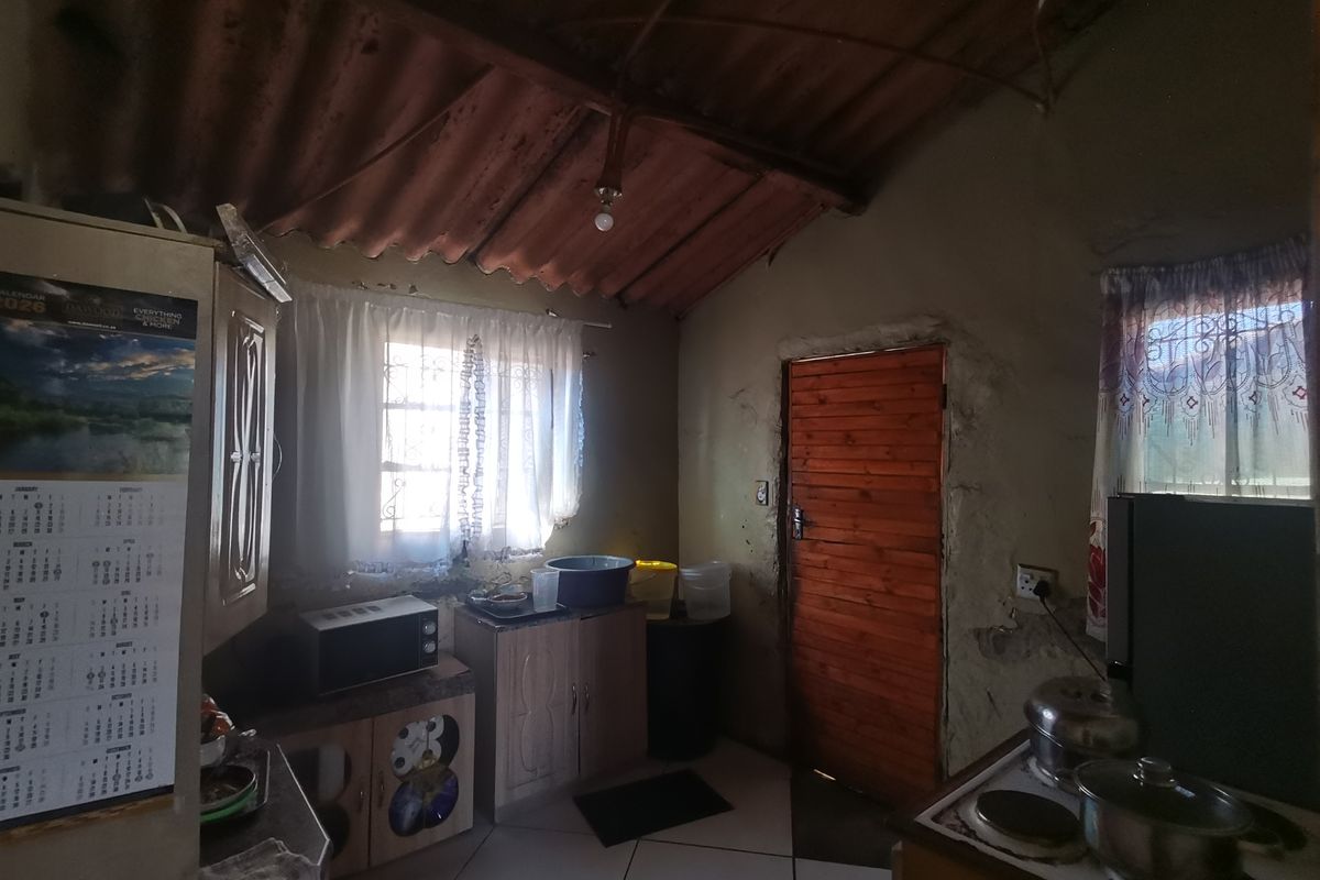 A rustic kitchen area featuring tiled floors, built-in cabinetry, and an exposed corrugated roof structure, requiring significant renovation to improve finishes and overall condition.
