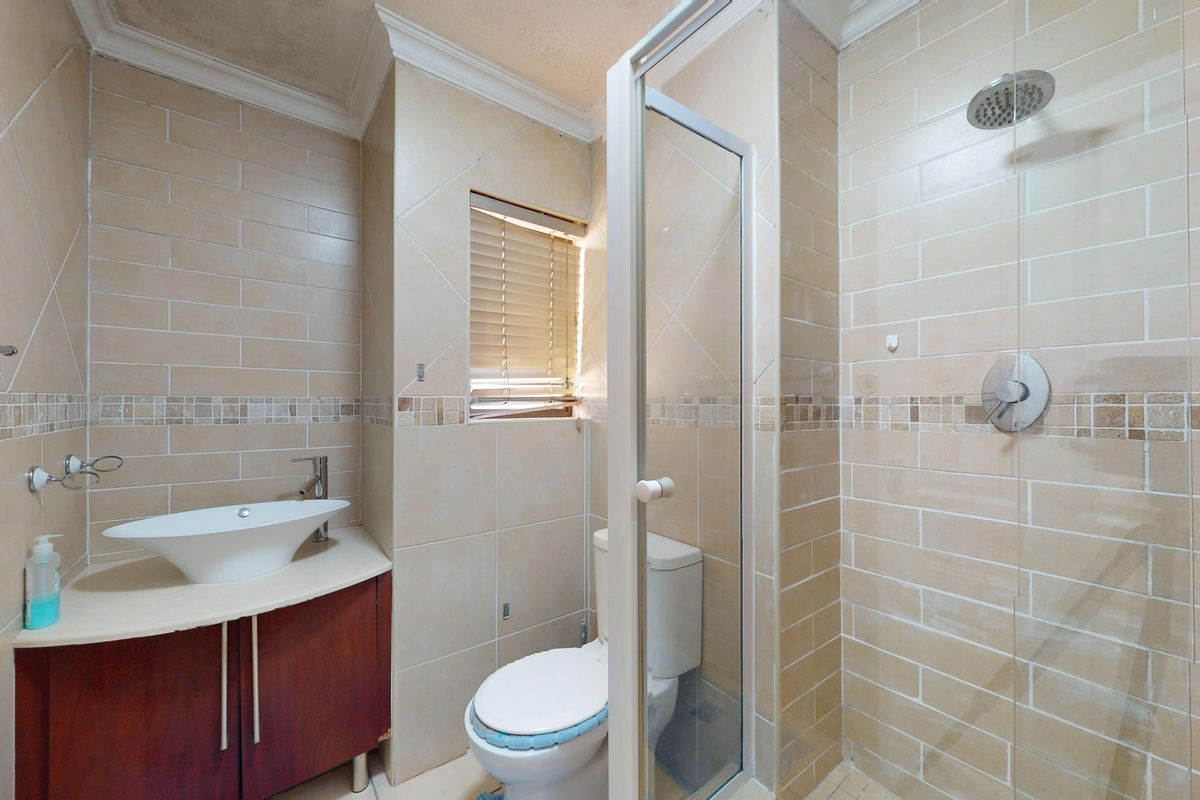 A functional bathroom featuring a vessel sink vanity, a glass-enclosed shower with a rain shower head, and neutral wall tiling.