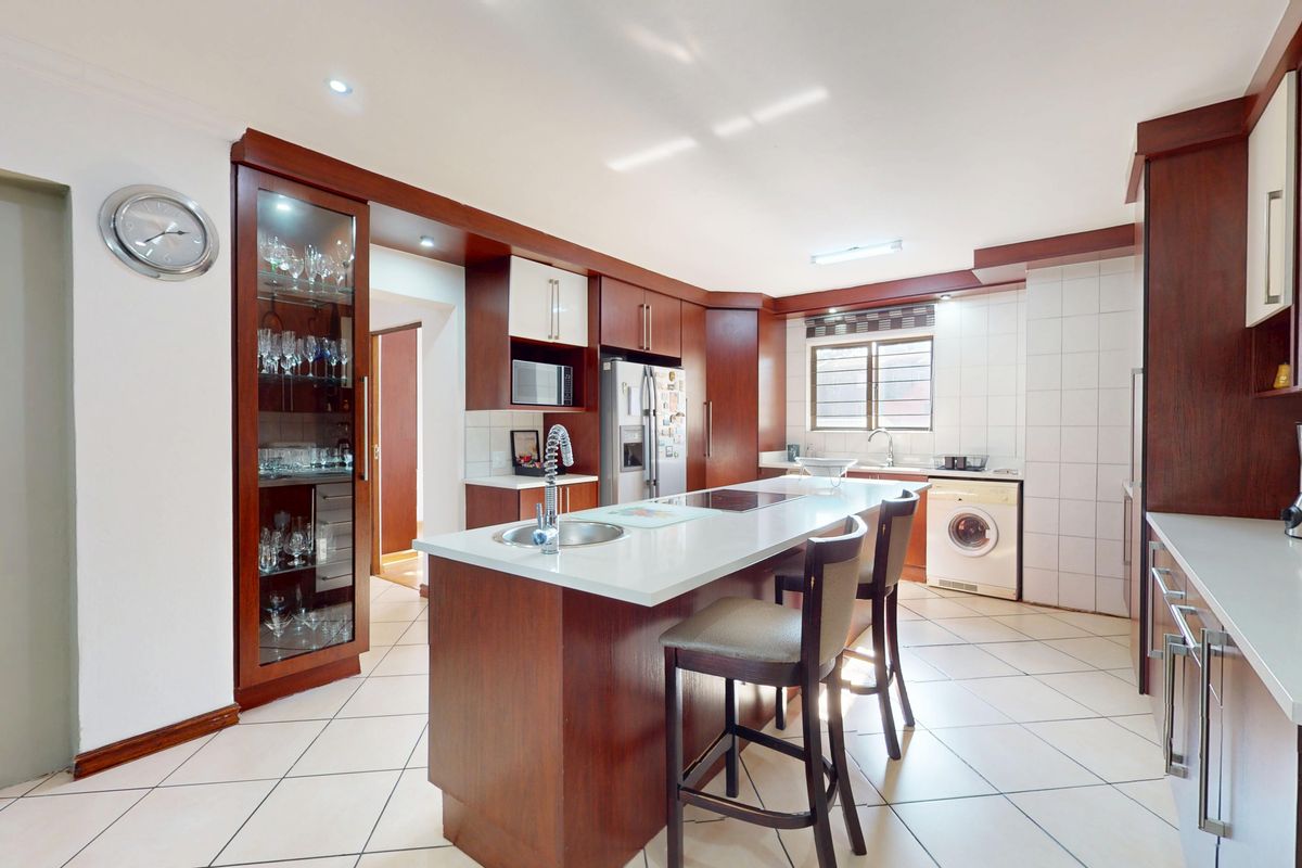 A well-appointed kitchen featuring dark wood cabinetry, a central island with a sink and cooktop, tiled flooring, and a built-in display cabinet.