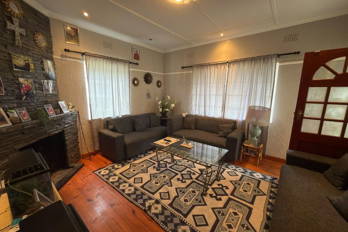 A cozy living room featuring a prominent stone-clad fireplace, warm hardwood flooring, and classic ceiling detailing, creating a comfortable and inviting atmosphere.