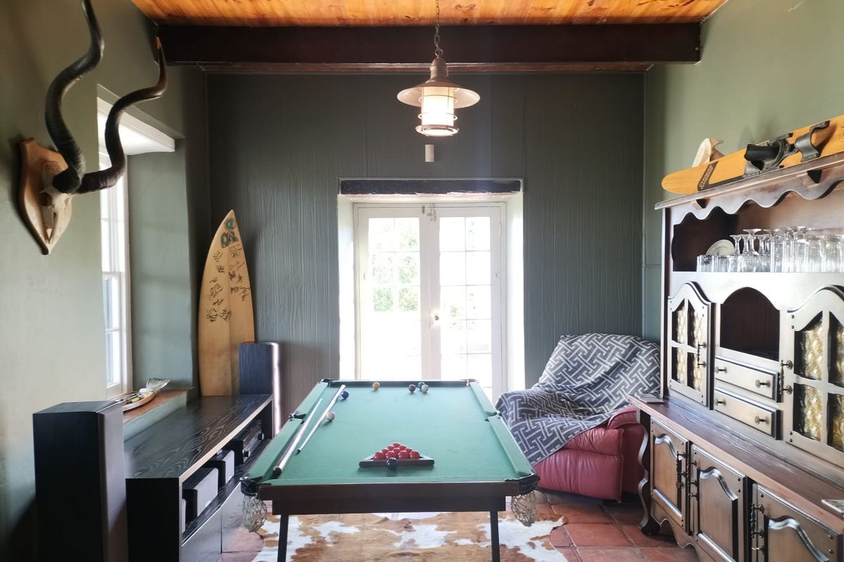A rustic entertainment room featuring exposed timber ceiling beams, terracotta floor tiles, and double glass doors leading to the exterior.