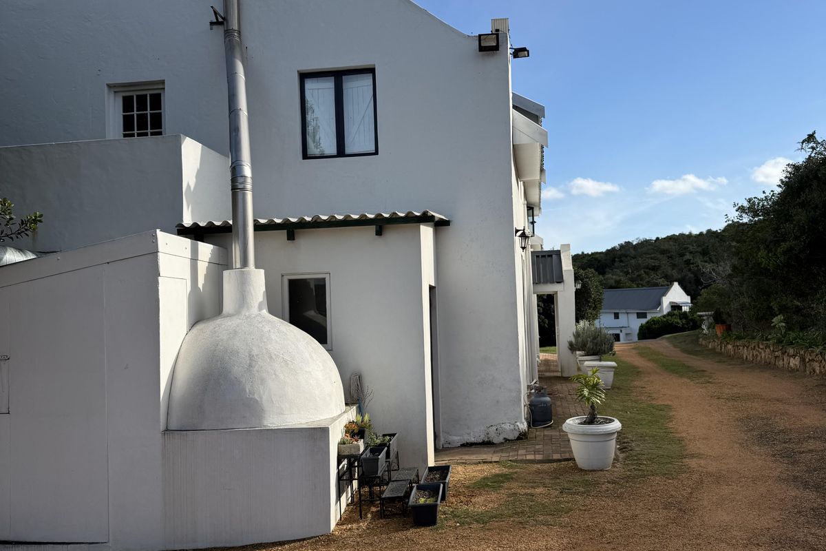 Side view of a white gabled guest house featuring an external fireplace with a tall chimney flue and gravel driveway access.