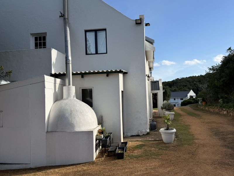 Side view of a white gabled guest house featuring an external fireplace with a tall chimney flue and gravel driveway access.