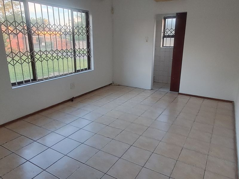 An empty living room featuring tiled flooring and security bars on the windows, providing a blank canvas for potential interior design updates.