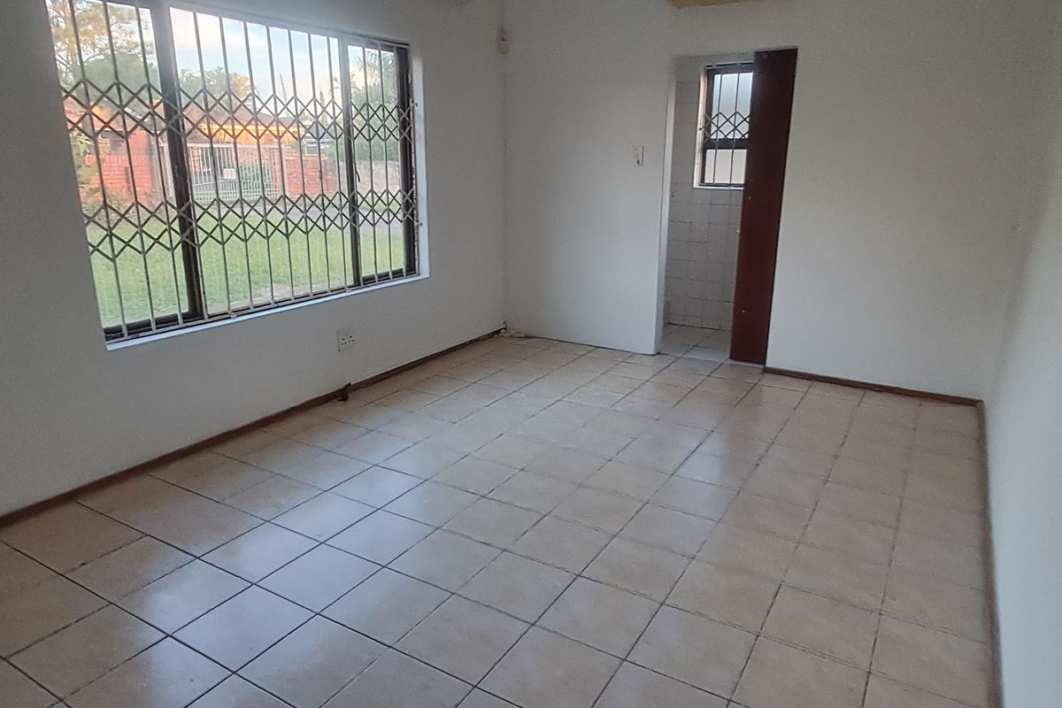 An empty living room featuring tiled flooring and security bars on the windows, providing a blank canvas for potential interior design updates.