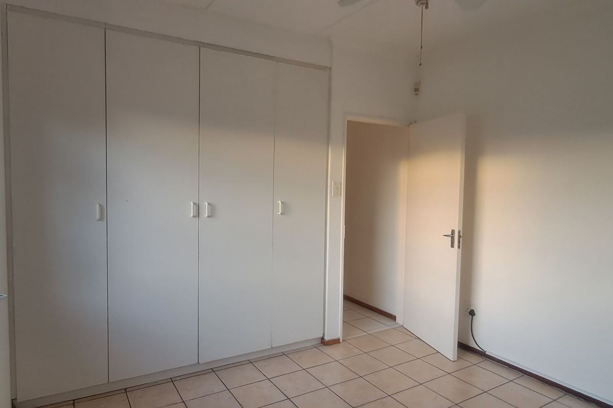 A bright, empty bedroom featuring built-in cupboards, tiled flooring, and a security gate on the window.