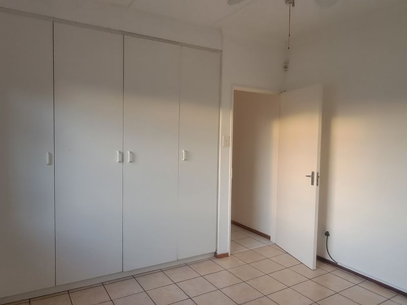A bright, empty bedroom featuring built-in cupboards, tiled flooring, and a security gate on the window.