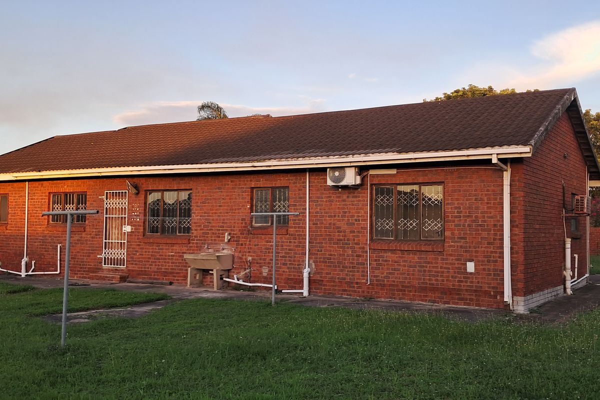 Rear view of a single-story brick house featuring a tiled roof, security bars on windows, and an external utility wash basin.