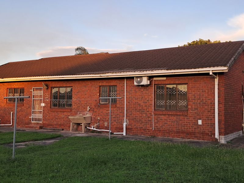 Rear view of a single-story brick house featuring a tiled roof, security bars on windows, and an external utility wash basin.