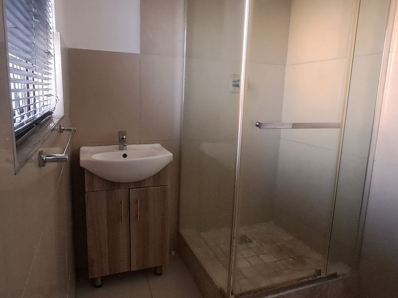 A functional bathroom featuring a vanity cabinet with a basin, a glass-enclosed shower, and neutral wall and floor tiling.