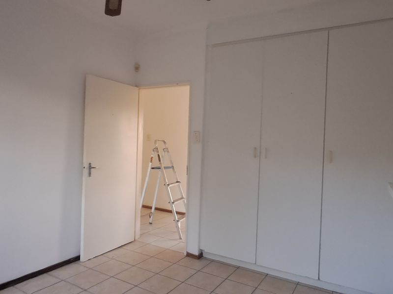 A simple, empty bedroom featuring built-in cupboards, tiled flooring, and a ceiling fan, offering a blank canvas for personalization.