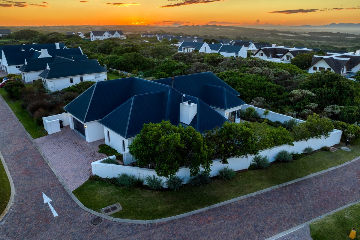 Aerial view of a residential property featuring a dark metal roof, brick paved driveway, and secure perimeter walling within a landscaped estate setting.