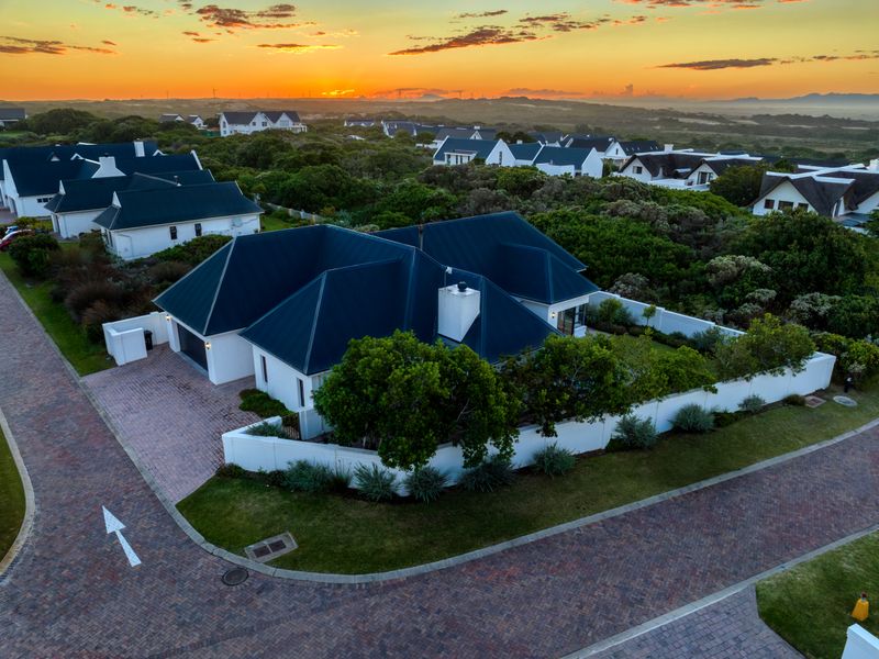 Aerial view of a residential property featuring a dark metal roof, brick paved driveway, and secure perimeter walling within a landscaped estate setting.