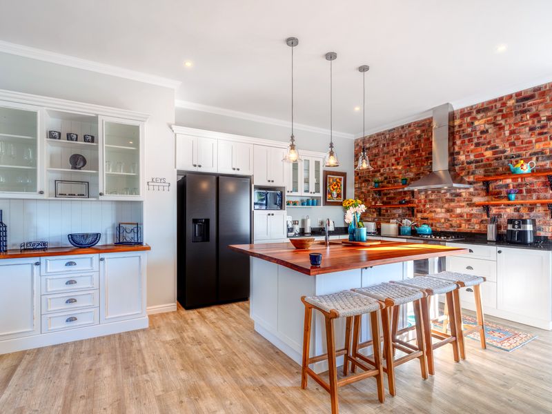 Modern kitchen featuring a large island with wooden countertop, exposed brick feature wall, white cabinetry, and high-quality pendant lighting.