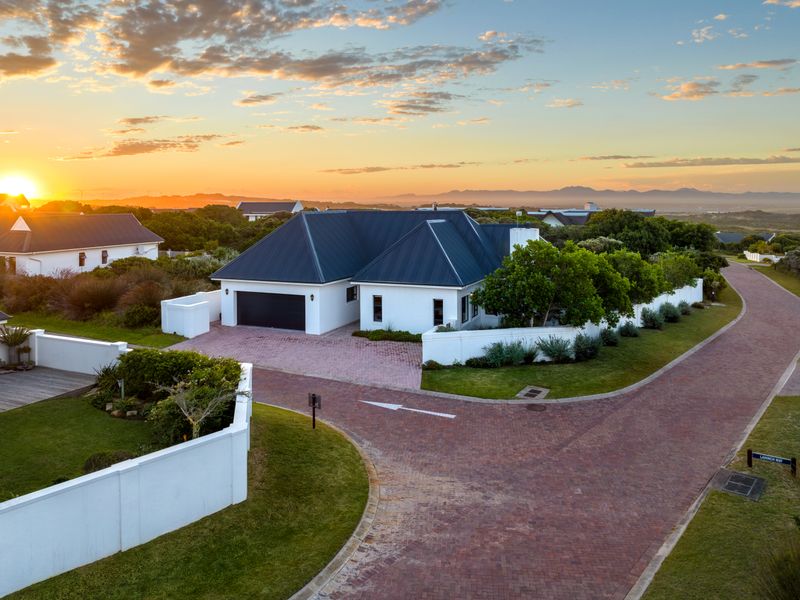 Aerial view of a well-maintained residential property featuring a metal roof, paved driveway, and landscaped garden at sunset.