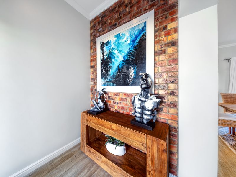 A well-maintained hallway featuring a striking exposed brick accent wall, complemented by modern laminate flooring and clean white finishes.