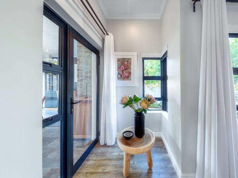 A bright, modern hallway featuring wood-look tile flooring and black aluminium framed glass doors and windows, providing a seamless transition to the living area.