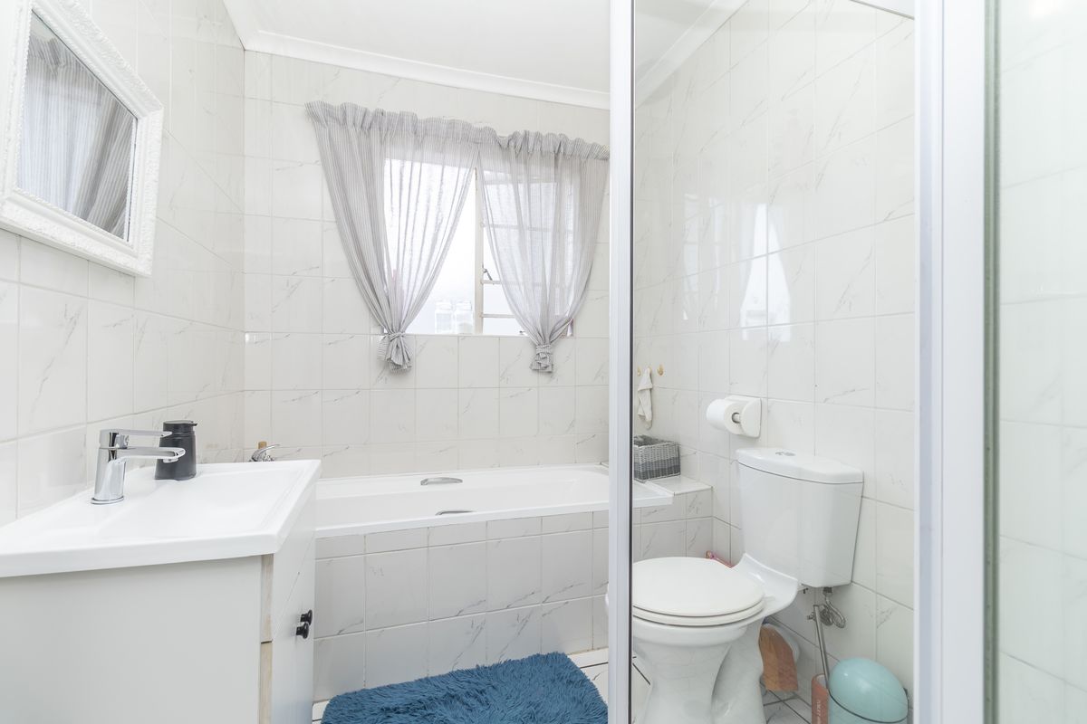 A functional bathroom featuring a built-in bathtub, a modern vanity unit, and a toilet, finished with white marble-look wall tiles.