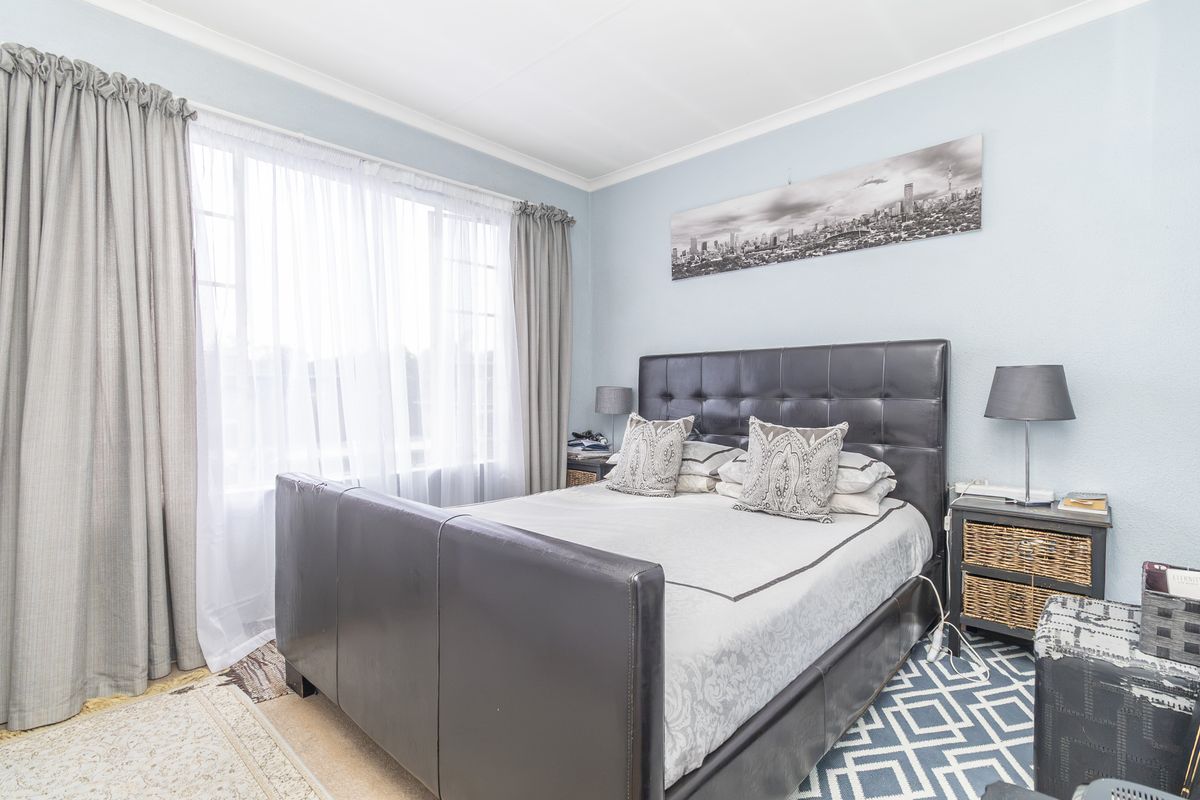 A well-lit bedroom featuring neutral wall tones, large windows with curtain tracks, and carpeted flooring.