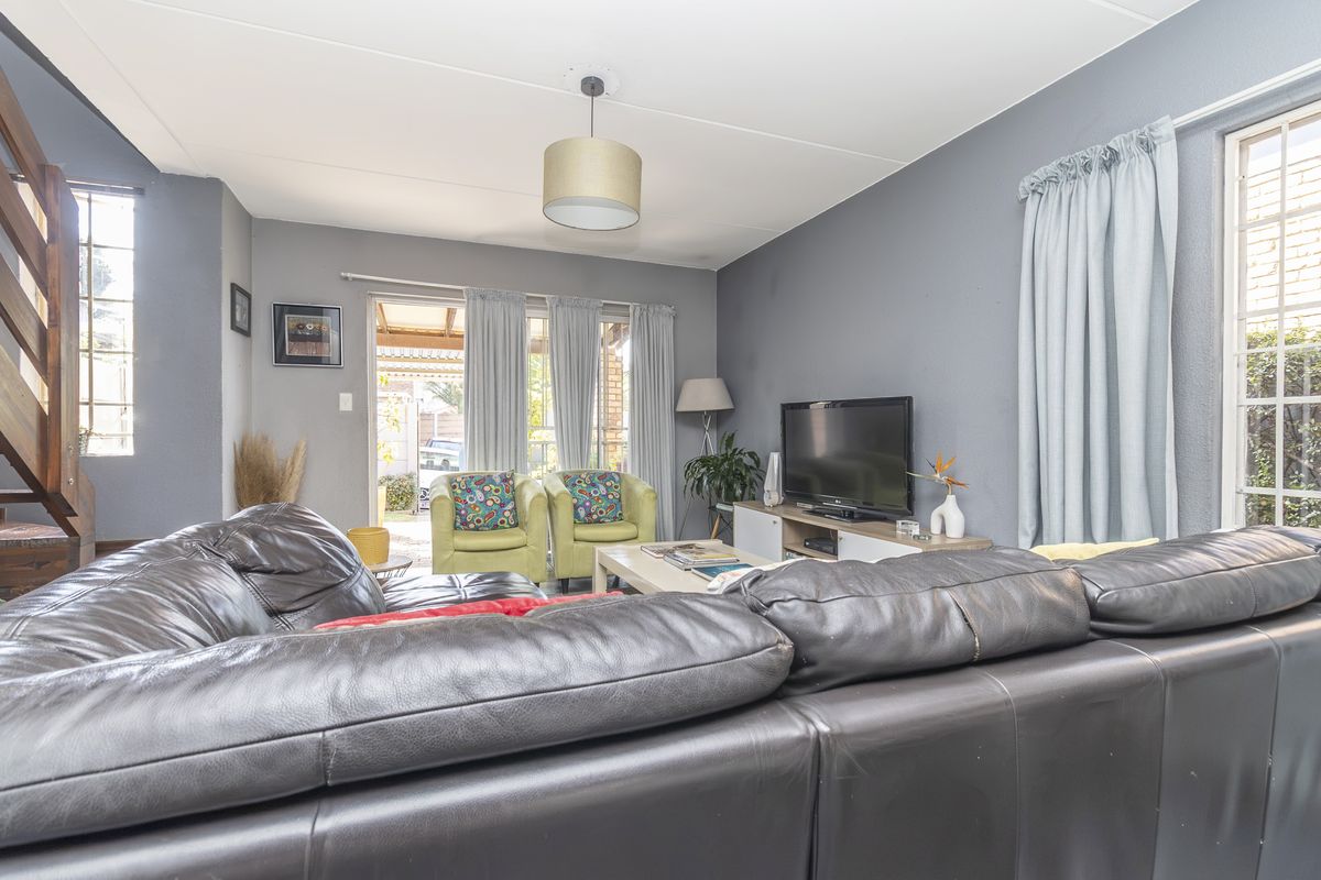 A comfortable living room featuring a wooden staircase, large windows, and direct access to an outdoor patio area.