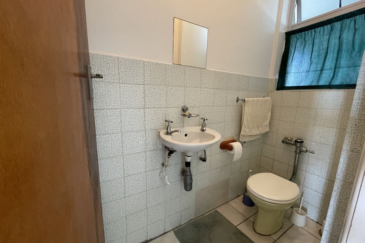 A compact bathroom featuring a wall-mounted basin, toilet, and tiled finishes, offering a functional space in need of cosmetic updates.