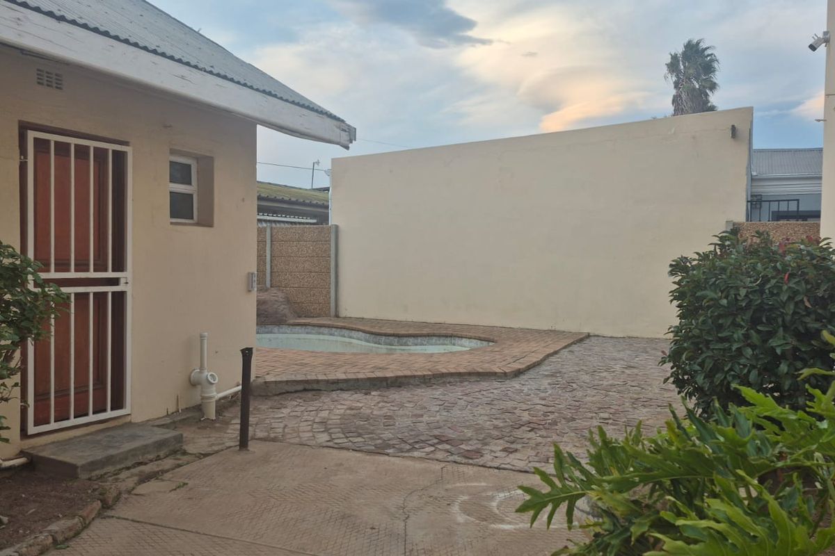 Rear exterior view featuring a small swimming pool, brick paved patio area, and high boundary walls for privacy.