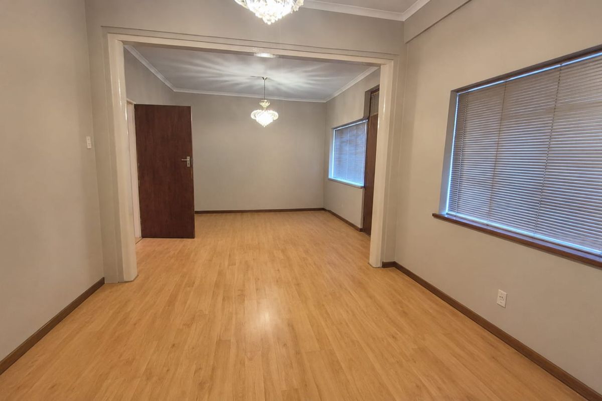 An empty, well-lit living area featuring laminate flooring, an open-plan archway, and classic crystal chandeliers.