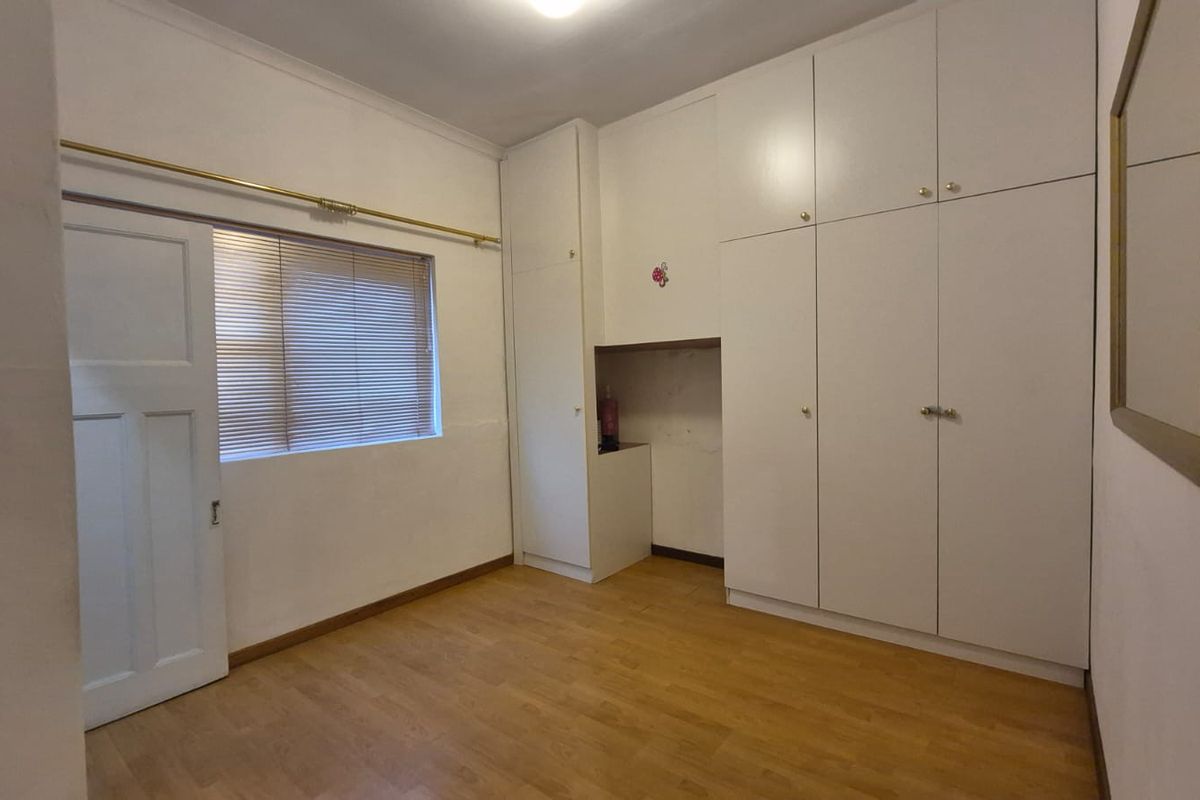 A vacant bedroom featuring laminate flooring, built-in floor-to-ceiling cupboards, and a window with fitted venetian blinds.