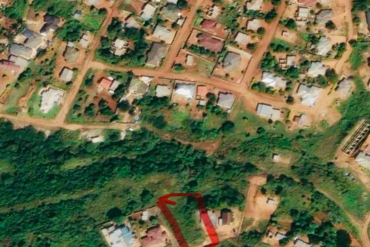 Aerial view of a vacant residential plot located within an established neighborhood, featuring direct access to an unpaved road.