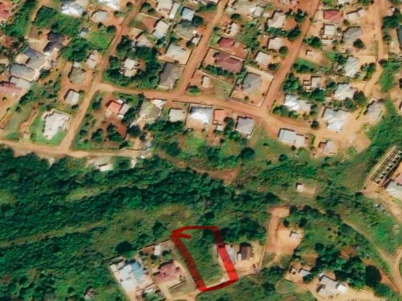 Aerial view of a vacant residential plot located within an established neighborhood, featuring direct access to an unpaved road.