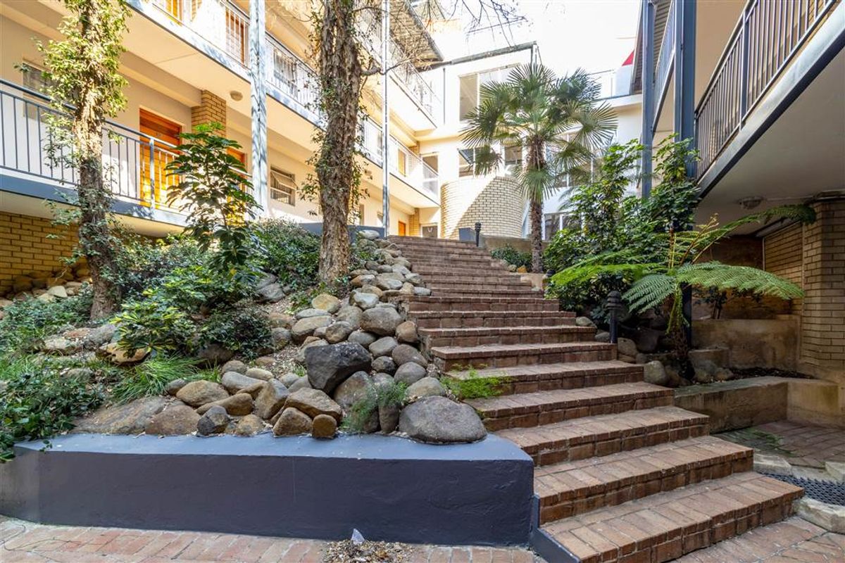 A landscaped courtyard area featuring a central brick staircase, rock garden, and surrounding apartment building facade with metal balcony railings.