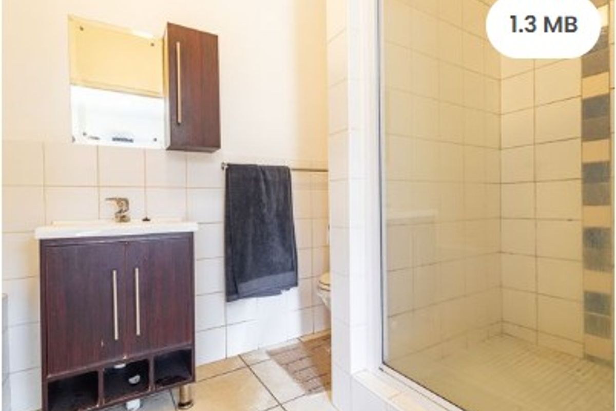A functional bathroom featuring a vanity cabinet with basin, wall-mounted storage, and a glass-enclosed shower with tiled finishes.